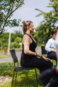 Vanessa als Yogalehrerin beim barrierefreien Yoga entspannt sitzend auf einem Stuhl in der Natur